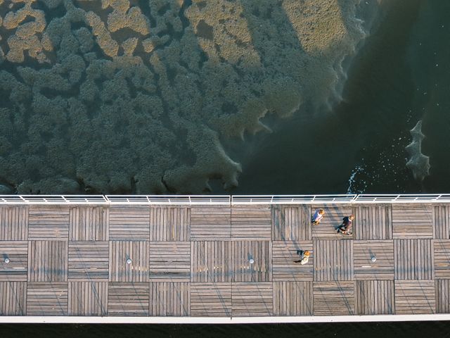 This overhead image shows a wooden boardwalk next to a body of water, with a few people walking. The picture captures shadows and textures, enhancing the natural environment. Ideal for use in articles, blog posts, or advertisements about outdoor activities, relaxation, nature walks, travel, and scenic views.