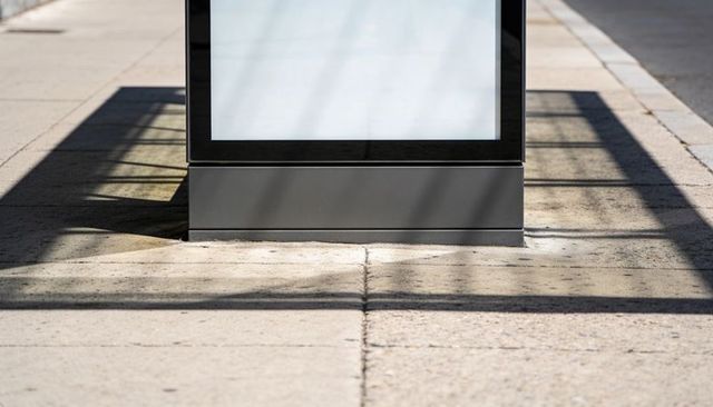 Freestanding advertising display standing on sunlit sidewalk casting bold linear shadows