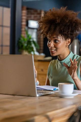 African american woman leading virtual meeting at cafe with laptop and coffee