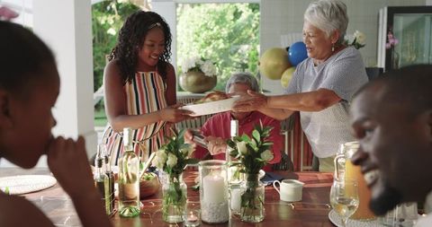 Multigenerational family sharing summer meal passing plate and smiling around dining table