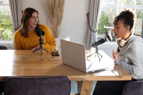 Women cohosting podcast at home recording on laptop using condenser microphones