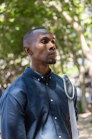 Thoughtful african american man standing on sunlit urban park walkway wearing navy shirt