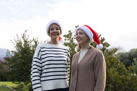Two friends wearing santa hats smiling in backyard garden for casual holiday portrait