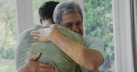 Senior father hugging adult son in sunlit doorway conveying warmth and tender reunion