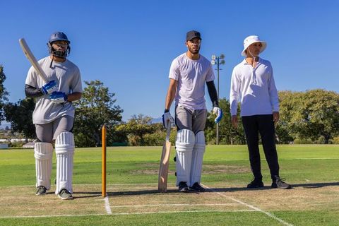 Diverse batsmen preparing for cricket match on sunny grass pitch