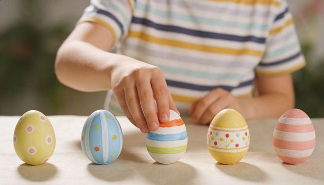 Child arranging pastel Easter eggs on table, colorful hand-painted egg row for spring craft