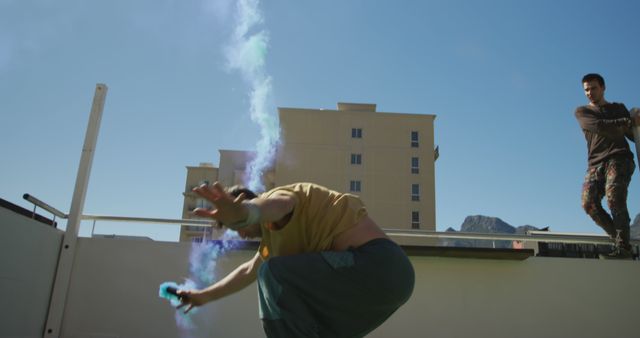 Young adults creatively expressing themselves with vibrant colored smoke on a rooftop. Great for projects showcasing urban culture, creative expression, or alternative arts. Suitable for use in advertisements, lifestyle articles, and marketing materials focused on street culture and youth engagements.