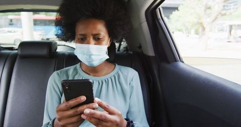 Businesswoman Wearing Face Mask Using Smartphone in Backseat