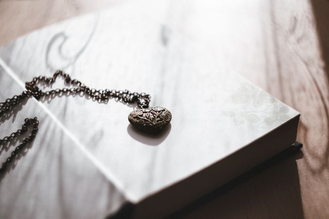 Delicate vintage heart locket chain placed on an open diary with soft sunlight casting shadows. Ideal for use in romantic, nostalgic, or sentimental themed projects including blogs, marketing materials, social media posts, and literature on antique jewelry or keepsakes.