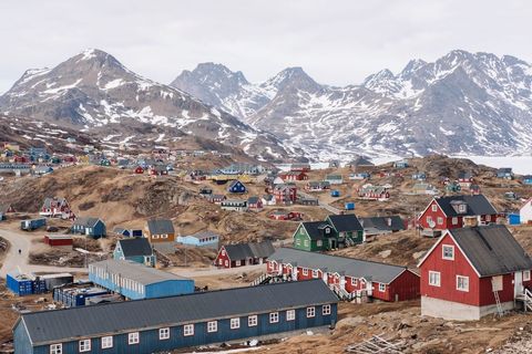 Stunning mountainous landscape with various colorful houses scattered in a Greenlandic village under cloudy sky. Shows rural living in a remote area whilst highlighting traditional architecture and northern landscape. Useful for articles or promotions about Greenlandic culture and lifestyle, or travel brochures showcasing arctic beauty and outdoor adventures.