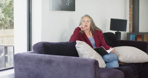 Mature woman relaxing on purple sofa with notebook in bright contemporary living room