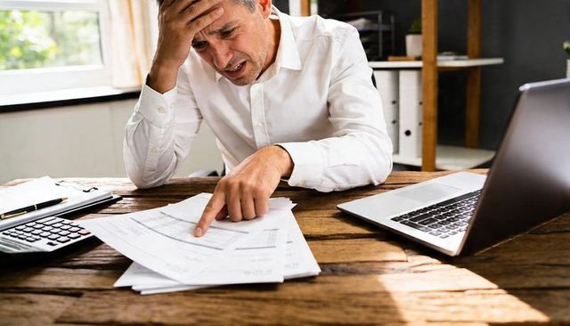 Stressed man pointing at bills while handling home office accounting and paperwork