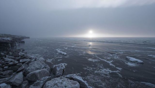 Misty frozen shoreline at dawn with snow-covered boulders and moody arctic sea