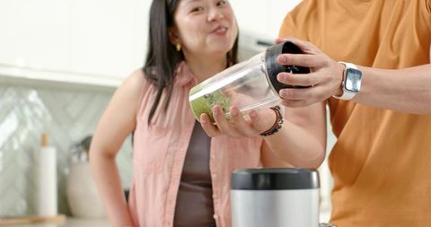Couple preparing green smoothie together in modern kitchen for healthy living and meal prep