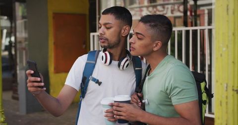 Two Male Friends enjoying Coffee Sharing Smartphone While Backpacking in City