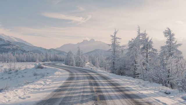 Winding snow-covered mountain road at dawn with frosted trees and tire tracks