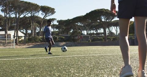 Youth soccer training on sunlit turf with teammate watching near goal and open field