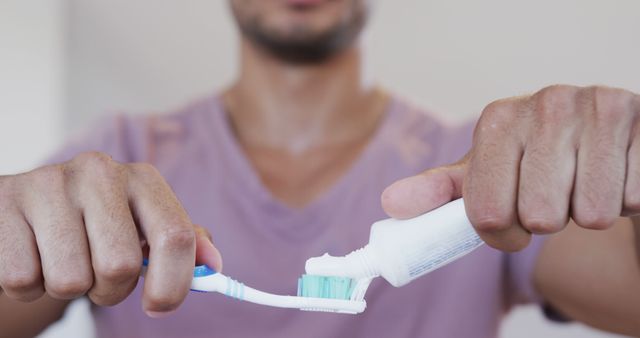 Man applying toothpaste to toothbrush in a close-up view, focusing on oral hygiene. Suitable for health and wellness content, dental care advertisements, and personal hygiene articles.