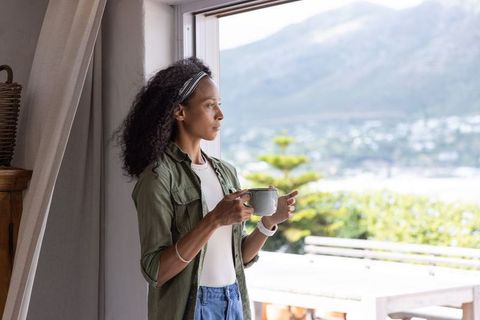 African american woman sipping coffee and gazing at mountain view from open doorway