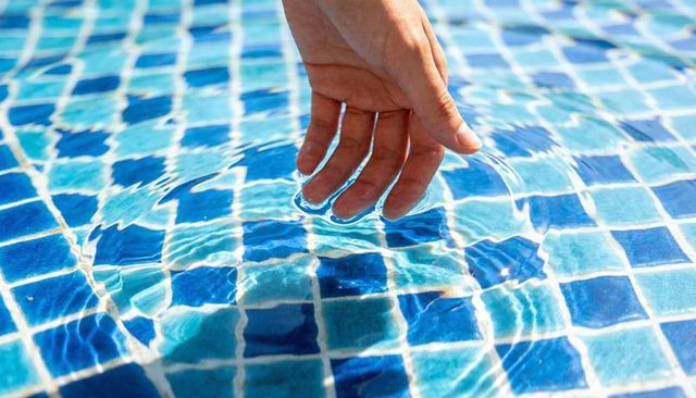 Sunlit hand dipping into pool water creating concentric ripples over blue mosaic tiles
