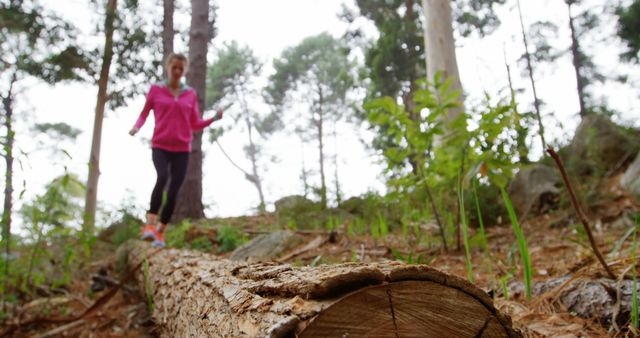 Woman balancing on a log in a forest, engaging in physical activity amidst nature. This can be used for content related to outdoor adventure, fitness, mental health benefits of nature, hiking activities, or balance and coordination exercises. Suitable for articles, blog posts, advertisements, or social media posts promoting healthy outdoor activities and fitness.