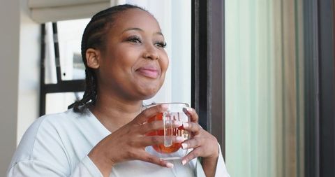 Serene african american woman enjoying tea by sunlit window, relaxing and gazing upward