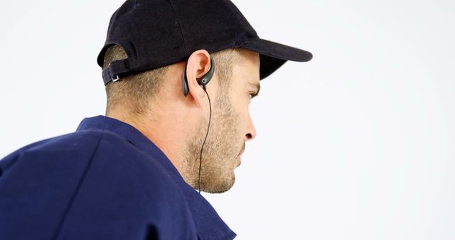 A Caucasian man wearing a cap and earphones is captured in profile, with copy space. His focused expression suggests he might be listening intently or concentrating on a task.