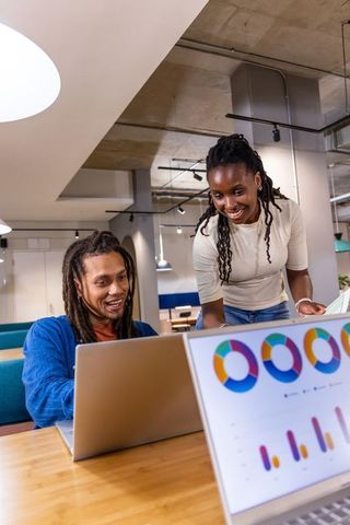 African American coworkers collaborating on laptop in coworking space with data charts