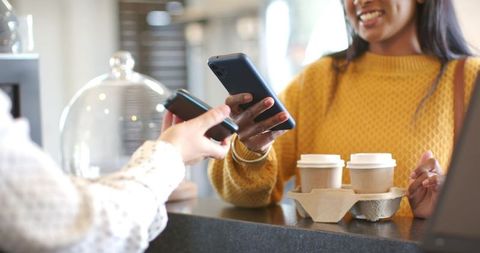 African american woman tapping phone for contactless coffee pickup at cafe counter
