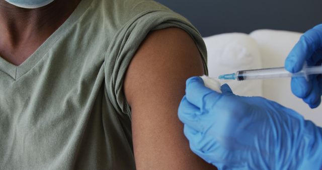 Close-up of a person getting a vaccine injection in the upper arm. Medical professional using blue gloves is administrating shot. Ideal for health-related content, immunization campaigns, medical blogs, or educational materials on vaccination importance.