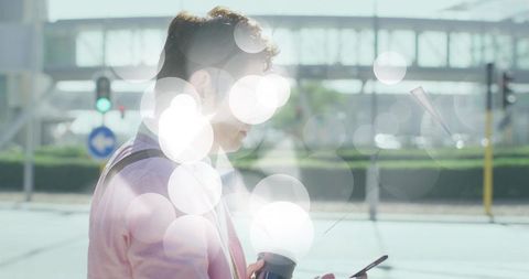Asian commuter checking phone while holding coffee near overpass with lens flare, city crosswalk