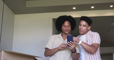 Two men comparing smartphone while unpacking new home