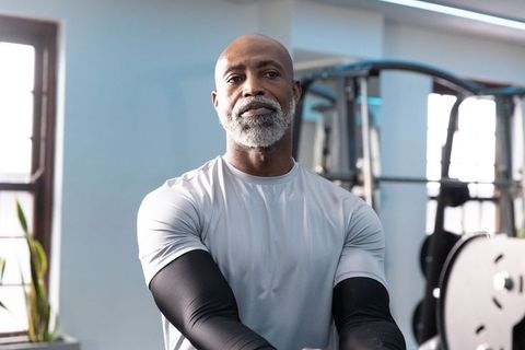 Senior african american man standing in gym beside power rack wearing gray athletic top