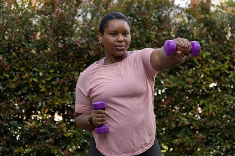 African american woman exercising with purple dumbbells in backyard lifting and training