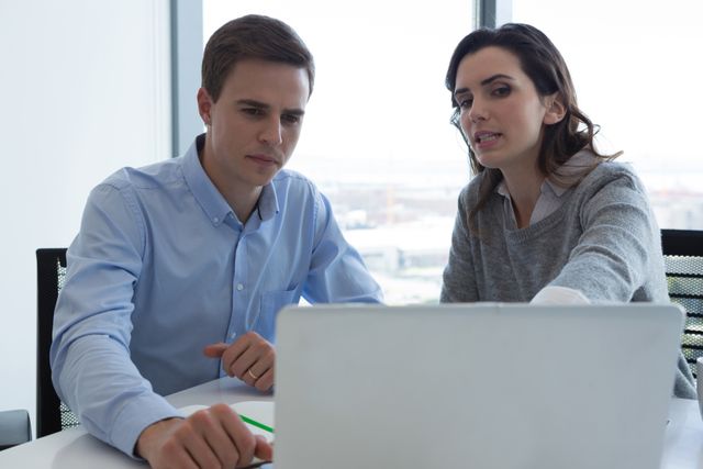 Male executive and female executive working over laptop in futuristic office