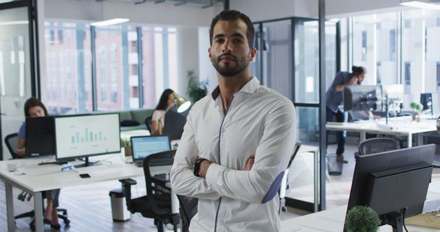 Portrait of biracial businessman standing in office smiling, with colleagues working in background. independent creative business in a modern office.