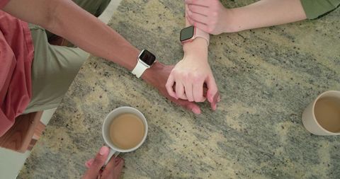 Couple holding hands over speckled granite countertop with smartwatches and coffee mugs