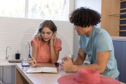 Couple planning morning over notebook at sunlit kitchen island, casual conversation