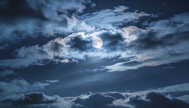 Full Moon Breaking Through Clouds with Radiant Moonlight Shafts and Halo Glow