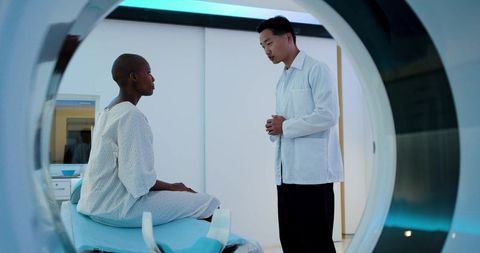 Patient consulting with radiologist beside mri gantry on scanner table in modern hospital