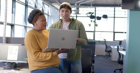 Diverse coworkers collaborating over laptop in modern open-plan office with natural light
