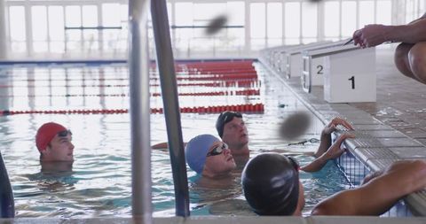 Competitive swimmers listening to coach at pool edge during indoor training session