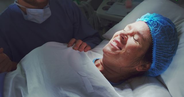 Mother lying in hospital bed smiling after successful childbirth while nurse or doctor stands by for support. Sunlight illuminates her face, conveying joy and relief. Ideal for use in maternity, healthcare, medical care, motherhood, and hospital related materials.