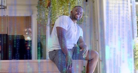 Smiling man sitting on wooden bench with code overlay, sunlit modern entry and greenery