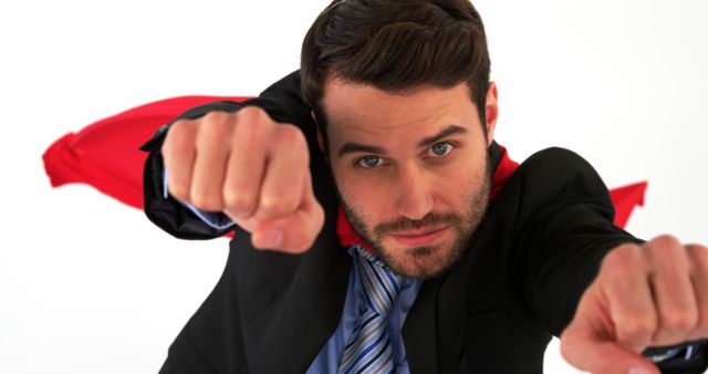 Adult man wearing a business suit and red cape pretending to fly in a superhero pose. The image portrays confidence, strength, and creativity, suitable for illustrating motivational articles, business presentations, and promotional materials. It can also be used to add a playful and dynamic element to corporate branding and advertisements.