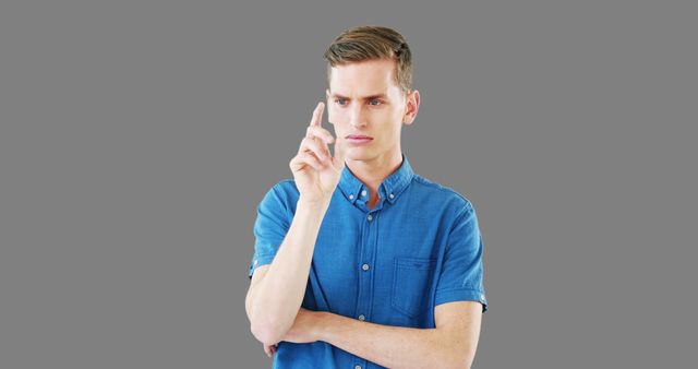 Young man in a blue shirt pointing his finger while appearing deep in thought. Useful for concepts like decision making, pondering, concentration, problem solving, and casual workforce.
