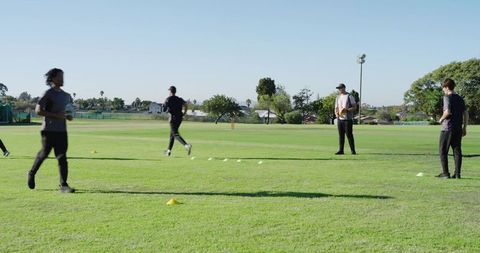 Team running drills on suburban grass field with cones and coach holding ball