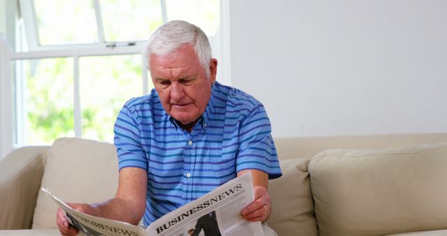 Mature man reading newspapers on sofa at home 