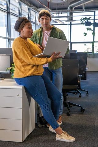 Diverse coworkers collaborating over laptop in modern industrial office with daylight