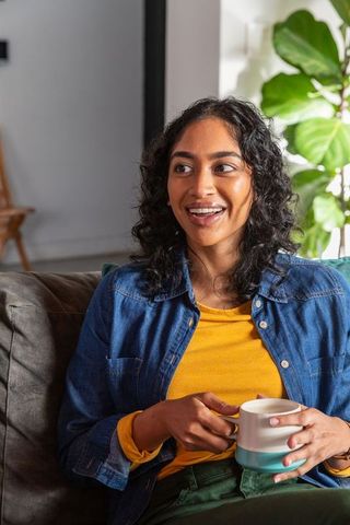 Cheerful Woman Relaxing with Coffee at Home by Foliage
